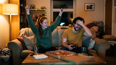 Photo 2: her cheering with her controller in the air while he covers his face