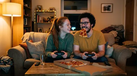 Photo 4: the couple side by side with their controllers, ready for another round