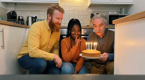 Photo 3: three coworkers hiding behind a counter with a cake